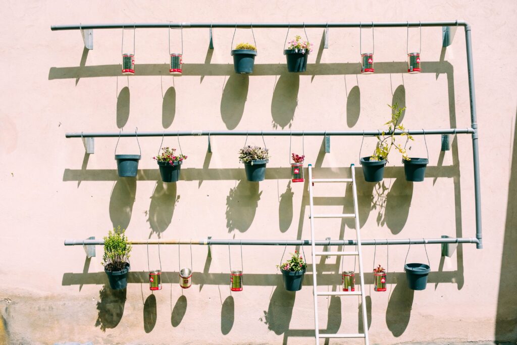 Starting a Vegetable Garden: Image showing a vertical garden made of PVC pipe and containers such as cans and small buckets with plants.